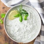 Bowl of Quark Dip viewed from the top garnished with herbs and sliced lemon on a wooden board and a grey and white napkin.