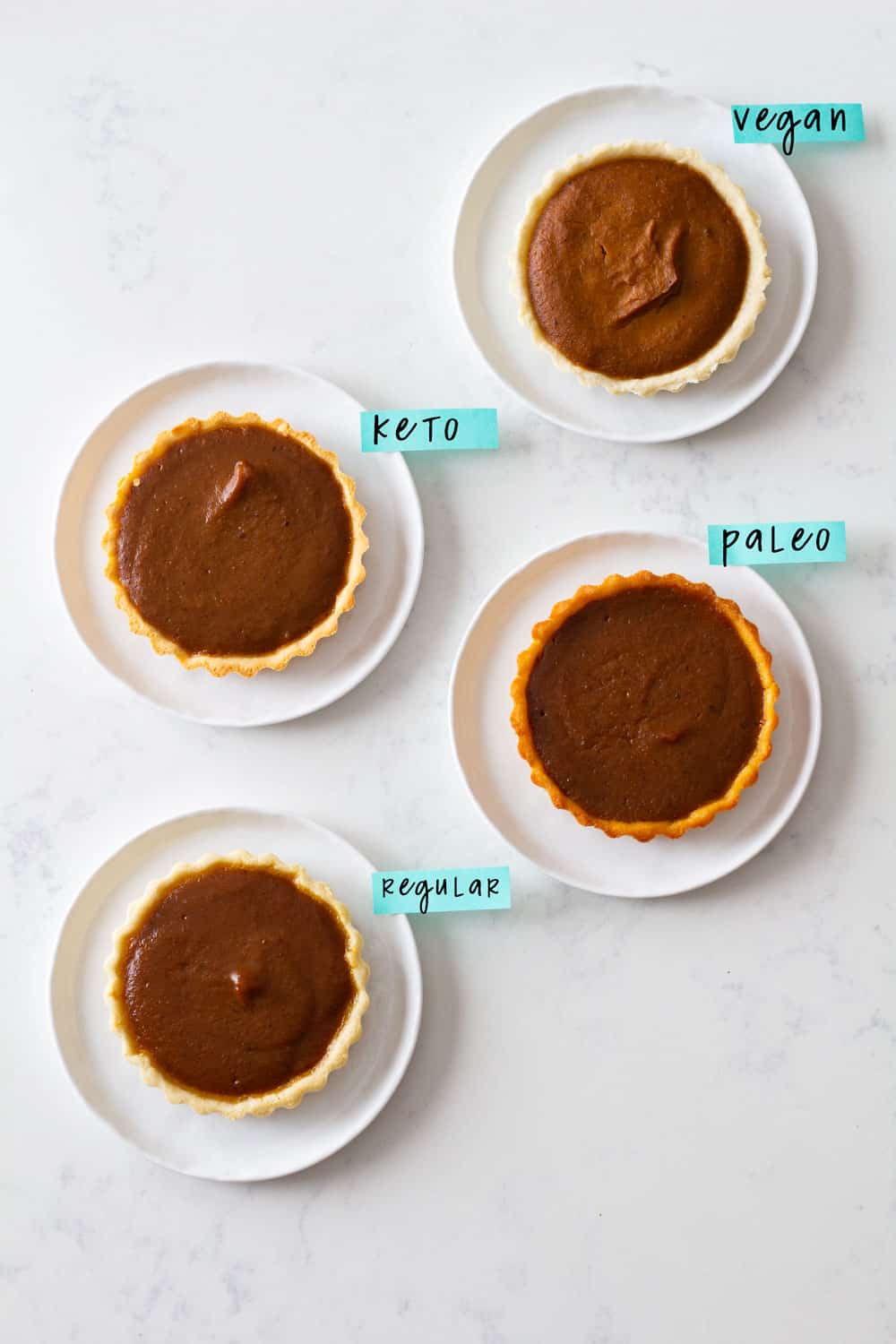 "Healthy" means a different thing for everybody. Why not be the nicest host ever and have a healthy pumpkin pie for everybody? Vegan Pumpkin Pie, Paleo Pumpkin Pie, Keto Pumpkin Pie and Regular Healthy Pumpkin Pie. Four different pumpkin pies on white plates: vegan, keto, paleo, and regular.
