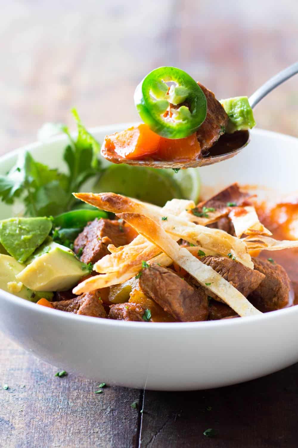 Mexican beef stew served in a white bowl and a spoonful of stew showing ingredients.