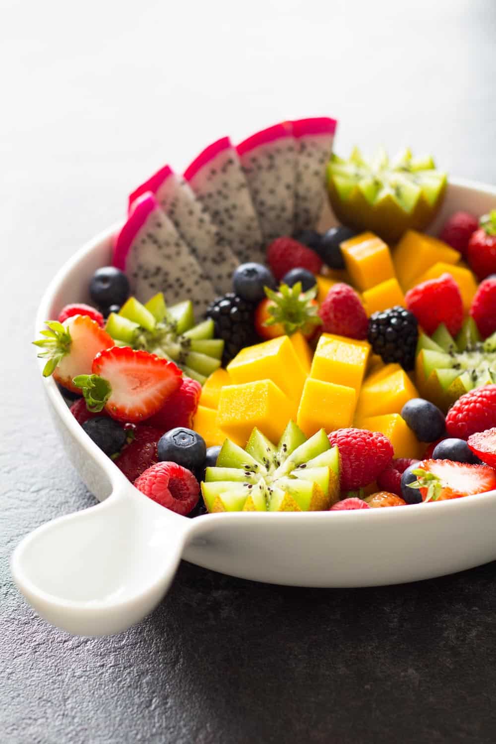 Fruit platter presented in a white bowl with a handle.
