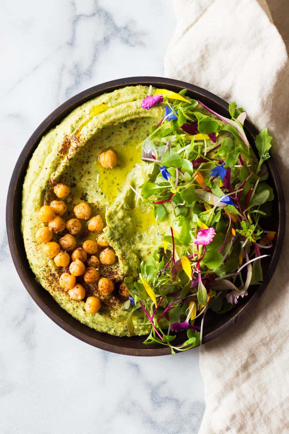 Top view of Spicy Avocado Hummus, with whole chickpeas and lettuce leaves sprinkled with chili powder.