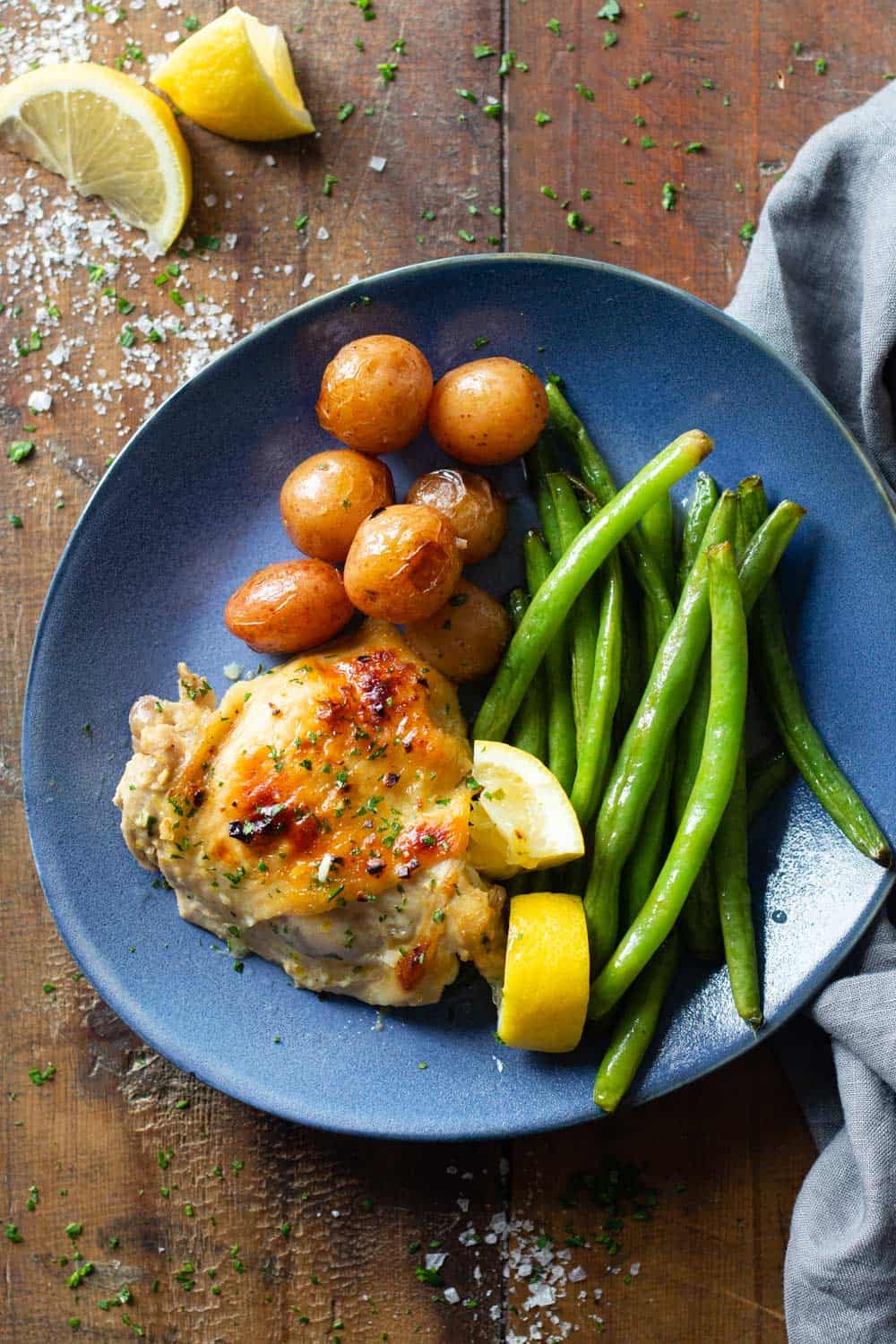 Lemon Garlic Chicken Thigh on a blue plate with potatoes and green beans
